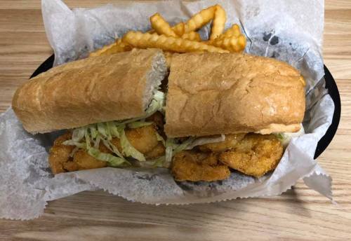 A sandwich filled with fried shrimp and lettuce, served with crinkle-cut fries on the side.