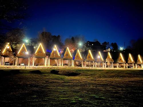 A row of cozy, illuminated A-frame cabins at night, set against a dark sky with stars.
