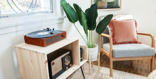 A cozy living space featuring a record player, vintage radio, potted plant, and a comfortable chair with a decorative pillow.