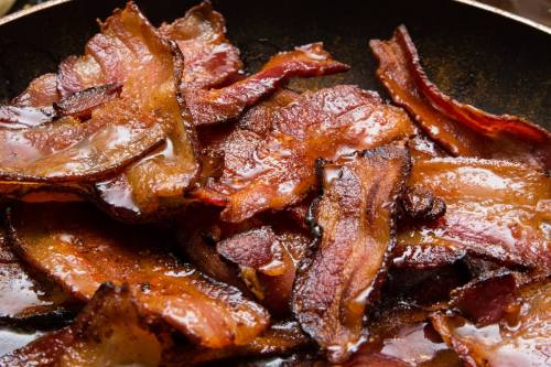 Crispy, golden-brown bacon strips sizzling in a frying pan.