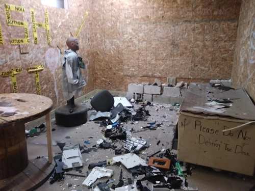 A cluttered room with scattered debris, a mannequin on a pedestal, and caution tape on the walls.