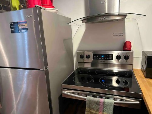 A stainless steel kitchen with a refrigerator, stove, and hood, featuring a colorful towel hanging from the oven.