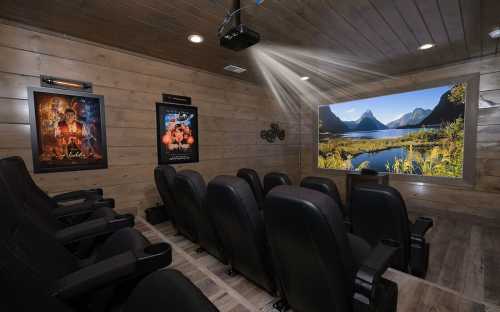 Home theater with black seating, wooden walls, a projector, and movie posters, featuring a scenic landscape on the screen.