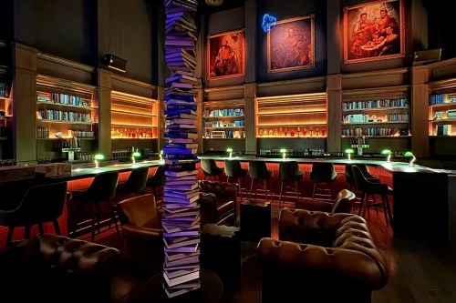 A stylish bar with a stack of books as a centerpiece, illuminated shelves, and cozy seating in a dimly lit atmosphere.