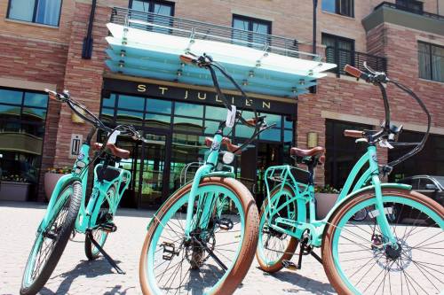 Three turquoise bicycles with brown accents parked in front of the St Julien hotel entrance.