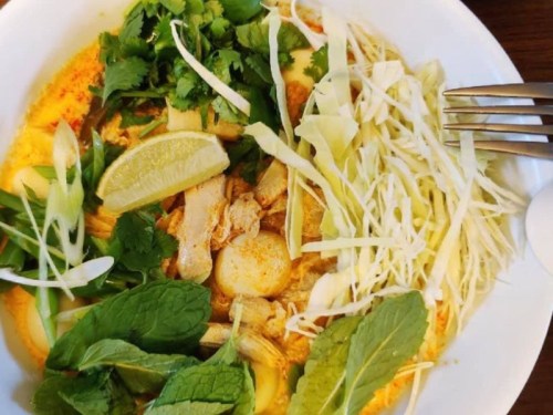 A bowl of vibrant noodle soup topped with chicken, lime, herbs, and shredded cabbage.