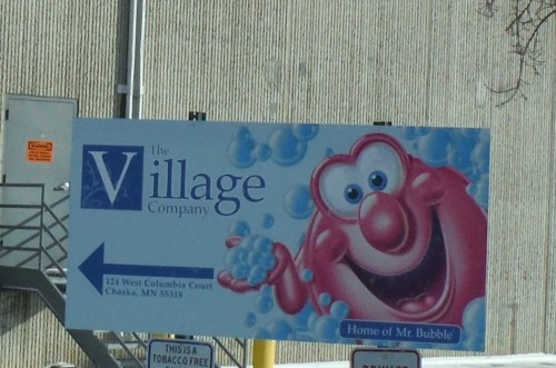 A colorful billboard featuring Mr. Bubble, promoting The Village Company in Chaska, MN.
