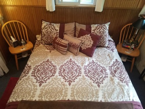 A neatly made bed with decorative pillows and a patterned blanket, flanked by two wooden side tables.