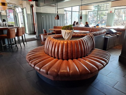 A modern restaurant interior featuring a circular leather booth and a potted plant centerpiece.
