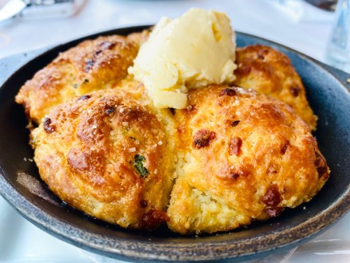 Golden, flaky biscuits served in a cast iron skillet, topped with a dollop of butter.