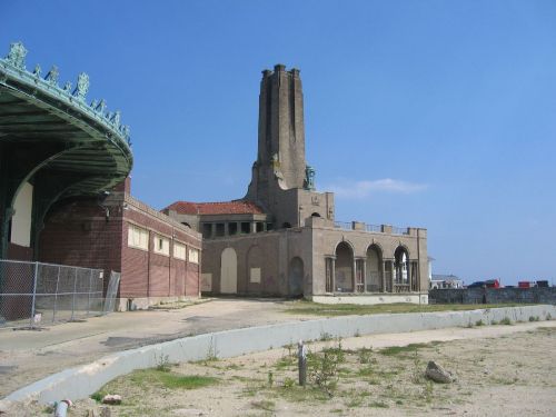 Abandoned building with tall chimneys, next to a vintage carousel structure under a clear blue sky.