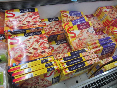 Frozen pizza boxes stacked in a freezer, featuring flavors like Calabresa and Pizza de Lombo.