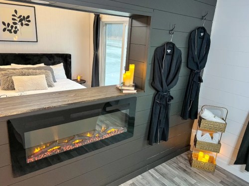 Cozy bedroom with a modern fireplace, black robes hanging, and soft lighting creating a warm atmosphere.