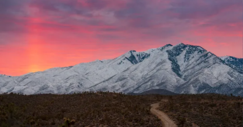 A snow-capped mountain under a colorful sunset, with a winding path in the foreground.