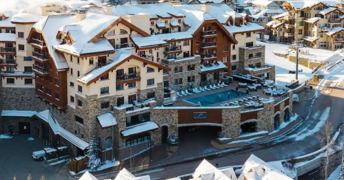 A snowy resort with a large stone entrance and multiple balconies, surrounded by winter scenery.