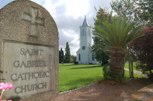 A stone sign reads "Saint Gabriel Catholic Church" with a white church and palm trees in the background.