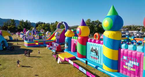A colorful inflatable bounce house park with various structures and people enjoying the attractions on a sunny day.
