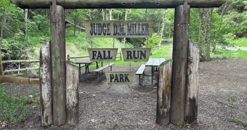 Wooden sign at park entrance reads "Judge D.M. Miller Fall Run Park," surrounded by trees and picnic tables.