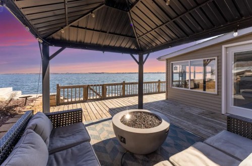 Cozy outdoor seating area with a fire pit, overlooking a serene lake at sunset.