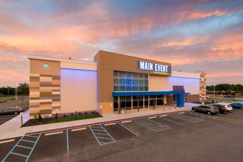 Exterior view of Main Event entertainment center at sunset, featuring modern architecture and a colorful sky.