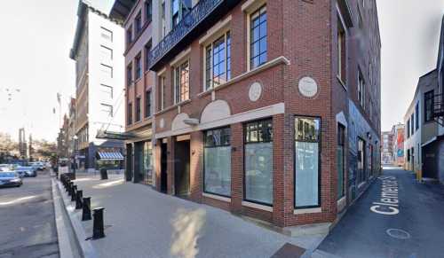 A brick building on a corner with large windows, decorative elements, and a street sign for Clemence Street.