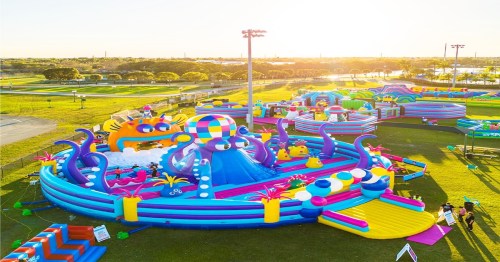 A colorful inflatable water park with slides and play areas, set in a sunny outdoor park.
