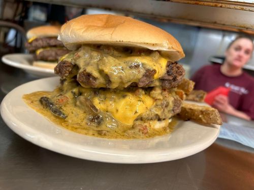 A close-up of a stacked cheeseburger with melted cheese and sauce, served on a plate with a side of bread.