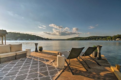 A serene lakeside view with lounge chairs, a small table, and a cozy seating area under a clear sky.