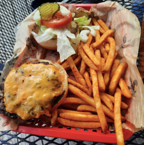 A basket with a cheeseburger topped with lettuce, tomato, and pickles, alongside a serving of sweet potato fries.