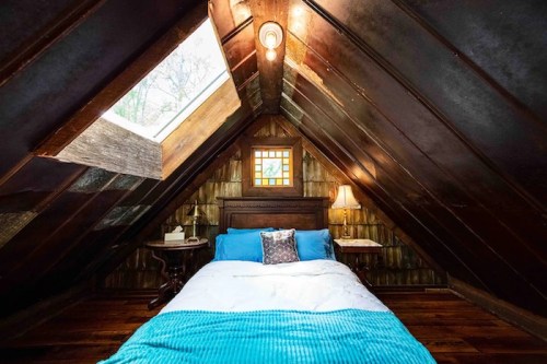 Cozy attic bedroom with a sloped wooden ceiling, skylight, blue bedding, and warm lighting.