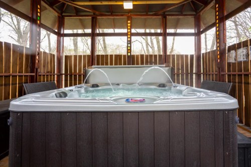 A hot tub with water jets, surrounded by wooden walls and seating, in a cozy outdoor gazebo setting.