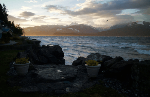 A serene lakeside view at sunset, with mountains in the background and gentle waves lapping at the shore.
