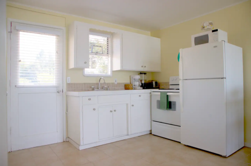 Bright kitchen with white cabinets, a refrigerator, stove, and a door leading outside. Light yellow walls enhance the space.