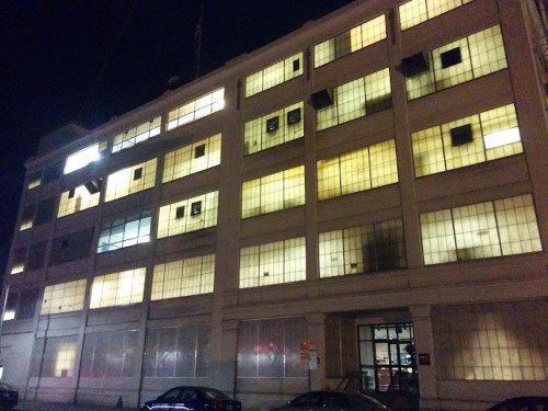 A dimly lit, multi-story building at night with illuminated windows and a few darkened areas.