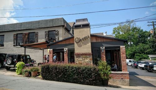 A cozy restaurant with a brick exterior and a sign reading "Chepers," surrounded by greenery and parked cars.