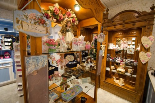 A cozy shop interior filled with decorative dolls, floral arrangements, and various collectibles on display.