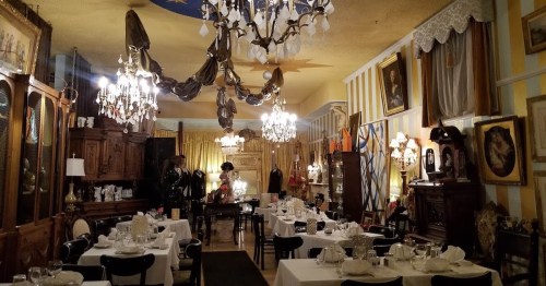 Elegant dining room with chandeliers, antique furniture, and decorative artwork, set for a formal meal.