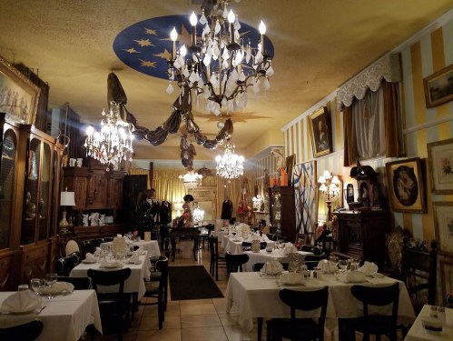 A cozy restaurant interior with elegant chandeliers, white tablecloths, and vintage decor, creating a warm atmosphere.