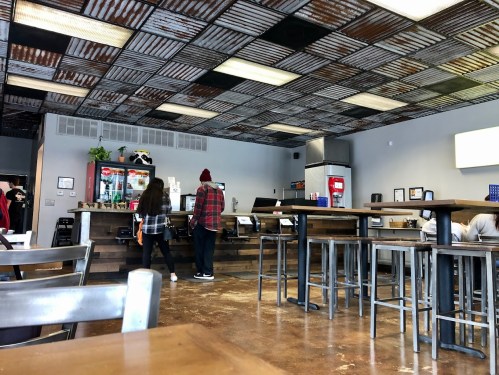 A casual café interior with metal tables, a rustic ceiling, and customers ordering at the counter.
