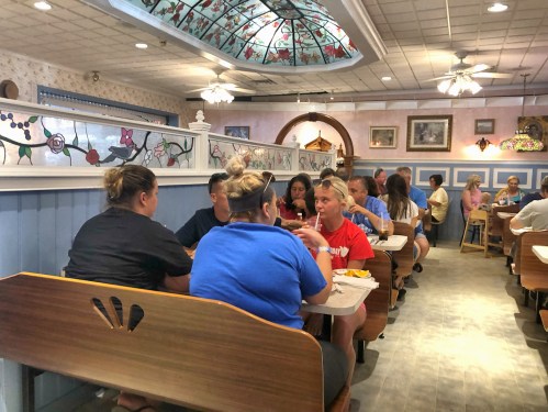 A busy restaurant interior with diners at tables, colorful decor, and a stained glass ceiling.