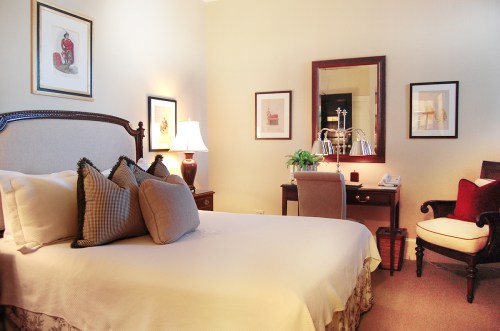 Cozy bedroom with a bed, desk, lamp, and framed artwork, featuring warm lighting and elegant decor.