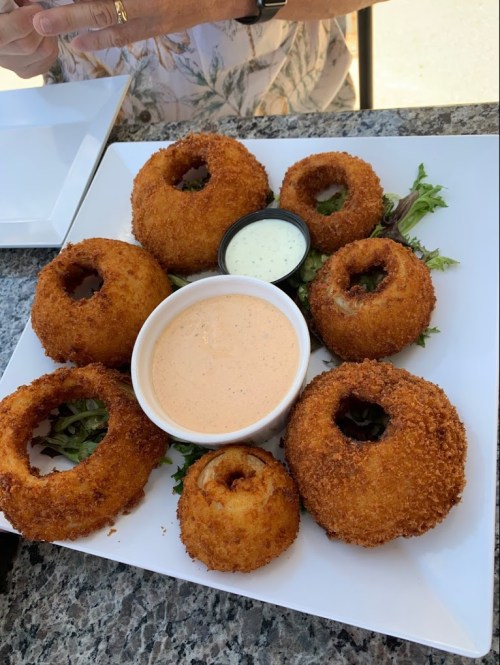 A plate of crispy fried onion rings arranged around a bowl of dipping sauce, garnished with greens.