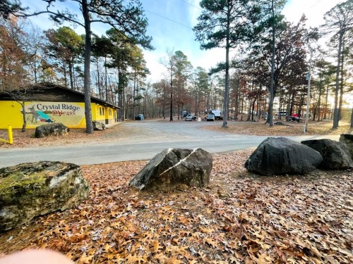 A view of a park entrance with a yellow building, surrounded by trees and large rocks, in a wooded area.