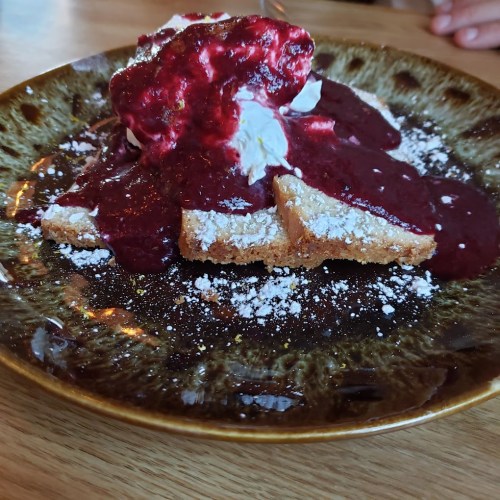 A plate of French toast topped with whipped cream and berry sauce, dusted with powdered sugar.