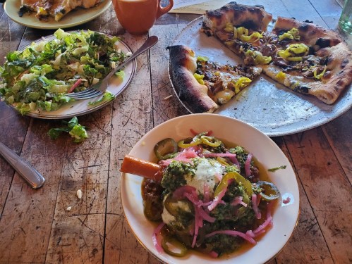A table with a plate of vibrant food, including a salad, a pizza, and a dish with green sauce and pickled onions.