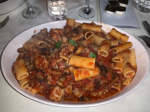 A large dish of rigatoni pasta with meat, mushrooms, and tomato sauce, garnished with fresh herbs.