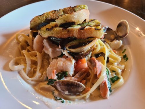 A plate of pasta with seafood, topped with grilled bread and garnished with herbs.