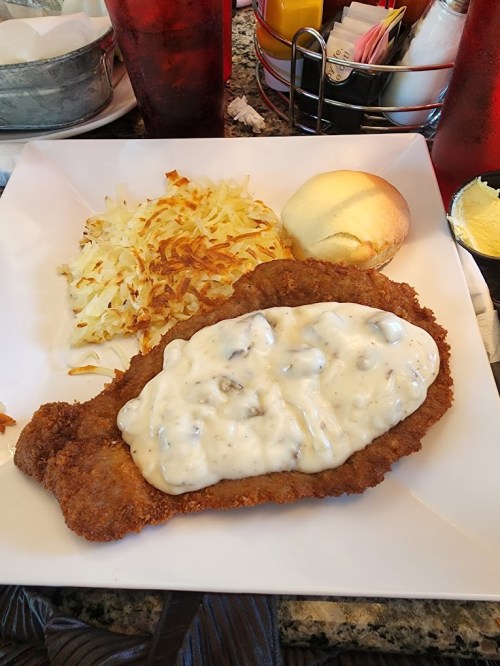 A plate featuring fried chicken with creamy gravy, hash browns, and a biscuit.