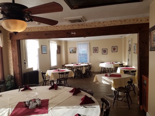 A cozy dining room with round tables set for meals, featuring yellow walls and decorative artwork.