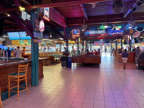 Interior of a vibrant food market with colorful neon signs, seating areas, and people enjoying their meals.